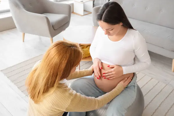 stock image Young pregnant woman with doula sitting on fitball at home