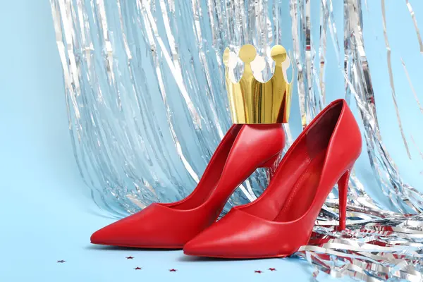 Paper crown with stylish red high heels and tinsel on blue background. Prom concept