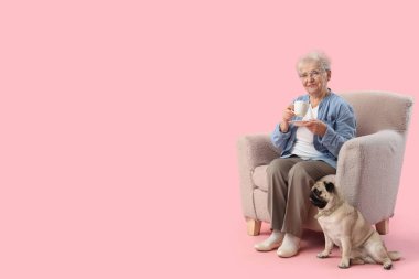 Bir fincan çay ve köpekli yaşlı kadın pembe arka planda koltukta oturuyor.