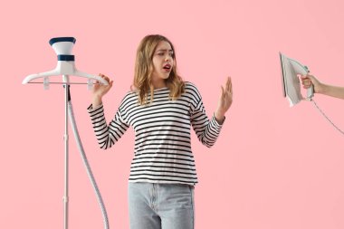 Pretty young woman preferring modern garment steamer over electric iron on pink background clipart