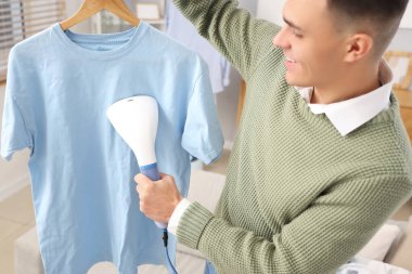 Mutlu genç adam evde buharlı mavi tişört giyiyor.