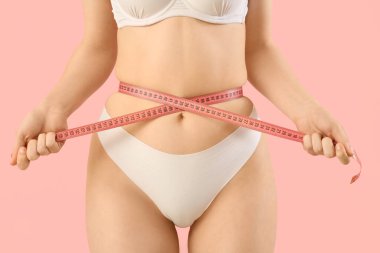 İç çamaşırlı, pembe arka planda mezurası olan güzel bir kadın. Selülit kavramı