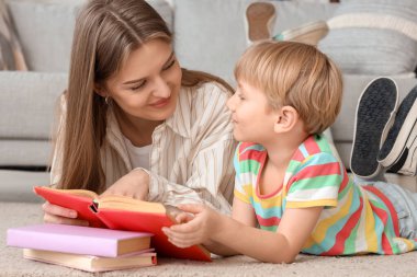 Küçük çocuk ve annesi evde yerde yatarken kitap okuyorlar.