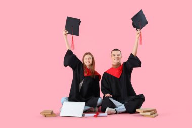 Diplomalı ve dizüstü bilgisayarlı yüksek lisans öğrencileri pembe arka planda havan tahtalarını yükseltiyorlar. Okul kavramının sonu