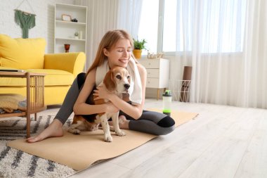 Sportif genç kadın, evde yoga yapan köpek üstüne sevimli Beagle 'a sarılıyor.