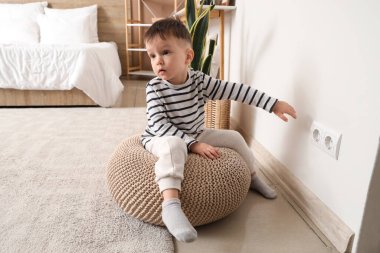 Yatak odasındaki elektrik prizinin yanındaki küçük çocuk. Tehlikedeki çocuk