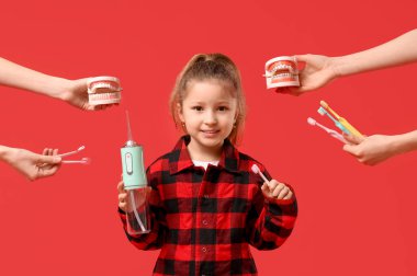 Ağız sulandırıcı tutan tatlı küçük kız ve elleri çene modelleri ve kırmızı arka planda diş fırçaları olan eller.