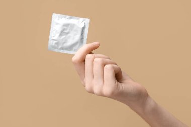 Kahverengi arka planda prezervatifli bir kadın el.