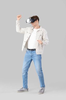 Young man using VR glasses on light background