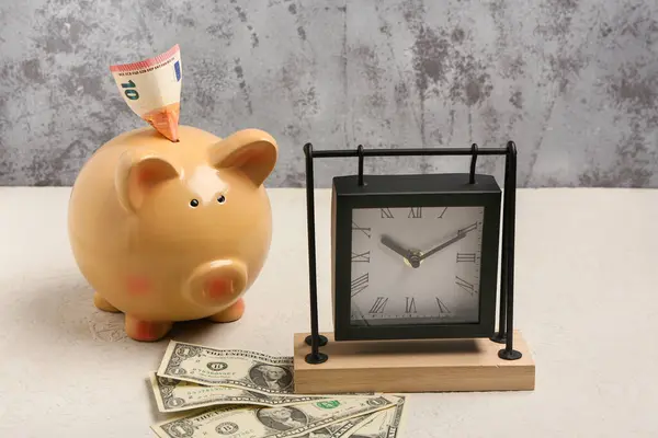 Composition with piggy bank, alarm clock and dollar banknotes on table against grey grunge background