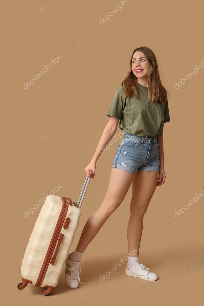 Beautiful young woman with suitcase on brown background