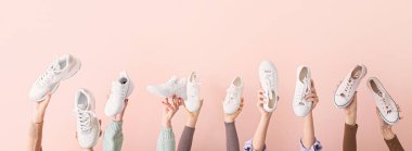 Pembe arka planda farklı spor ayakkabıları olan kadın elleri.