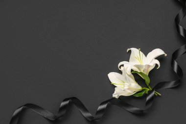 Koyu arkaplanda siyah cenaze kurdelesi olan güzel zambak çiçeklerinden yapılmış çerçeve.