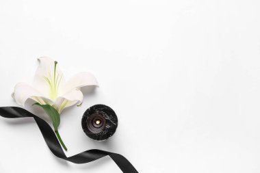 Güzel zambak çiçeği, yanan mum ve beyaz arka planda siyah cenaze kurdelesi.