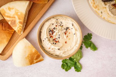Beyaz arka planda pide ekmeği olan bir kase lezzetli humus.