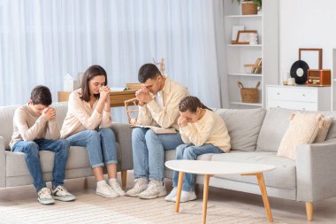 İncil 'i olan bir aile evdeki kanepede dua ediyor.