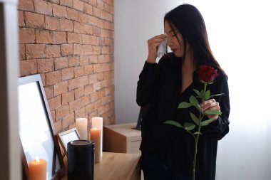 Grieving young Asian woman with rose and mortuary urn at funeral clipart