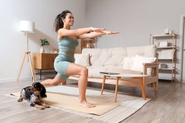 Cocker Spaniel 'le evde yoga yapan Afro-Amerikan bir kadın.