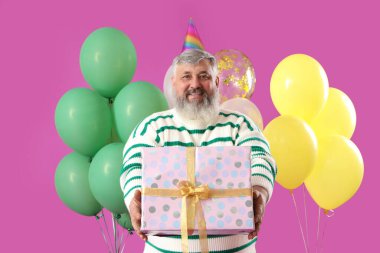 Hediye kutusu ve pembe arka planda bir sürü balonu olan son sınıf öğrencisi.