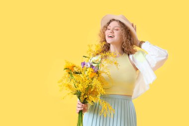 Sarı arka planda güzel çiçeklerle dolu buketi olan mutlu genç bir kadın.