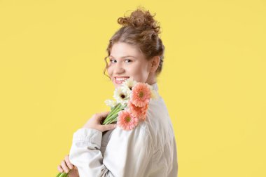Sarı arka planda güzel Gerbera çiçekleri olan mutlu genç bir kadın.