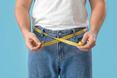 Mavi arka planda, belinde mezura olan genç bir adam, yakın plan. Kilo verme konsepti