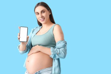 Mavi arka plandaki aşıdan sonra cep telefonu ve tıbbi yaması olan hamile bir kadın.