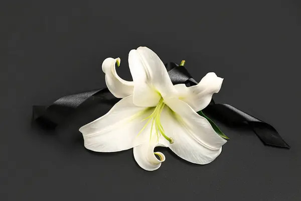 Beautiful lily flowers with black funeral ribbon on dark background
