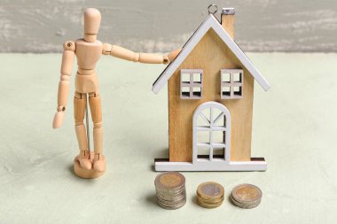 Ahşap insan figürlü kompozisyon, ev figürü ve masanın üzerinde grunge arka planda duran madeni paralar. Zaman yönetimi kavramı