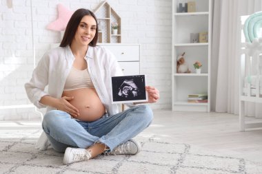 Çocukların yatak odasında ultrason görüntüsü olan hamile bir kadın var.