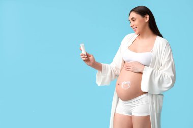 Genç hamile bir kadın krem sürmüş mavi arka planda çatlaklar var.