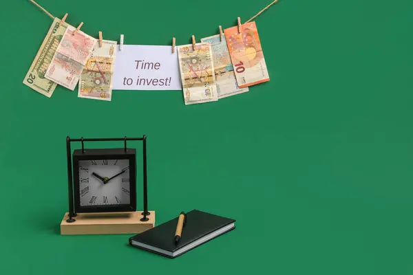 Paper with text TIME TO INVEST, money and alarm clock on green background