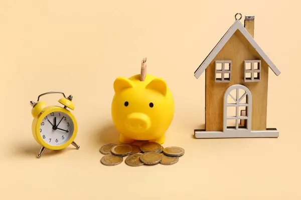Composition with piggy bank, alarm clock and house figure. Time management concept