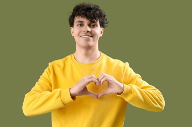 Yakışıklı genç adam, elleri yeşil arka planda kalp yapıyor.