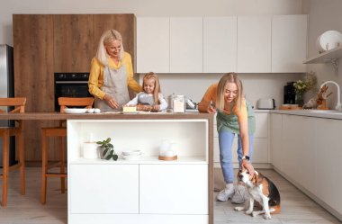 Annesi ve büyükannesiyle küçük tatlı bir kız mutfakta hamur hazırlıyor.