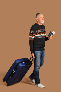 Kahverengi arka planda bavulu, pasaportu ve bileti olan yaşlı bir adam.