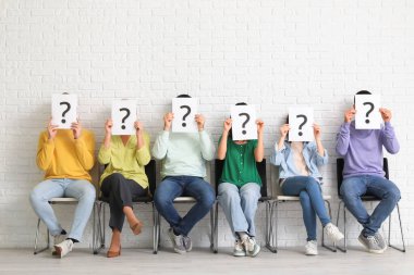 Adaylar beyaz tuğla duvarın yanında soru işaretli kağıt kağıtlar taşıyorlar