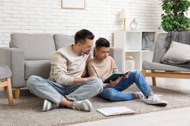 Baba ve küçük oğlu evde yerde kitap okuyorlar.