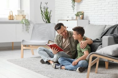 Baba ve küçük oğlu evde yerde kitap okuyorlar.