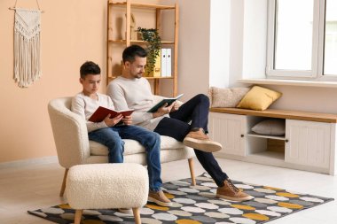 Baba ve küçük oğlu evdeki kanepede kitap okuyorlar.