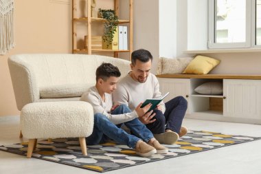 Baba ve küçük oğlu evde yerde kitap okuyorlar.