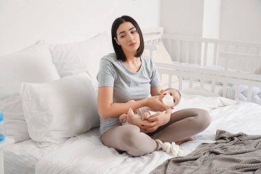 Depresyondaki genç kadın bebeğini yatak odasında besliyor.
