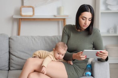 Evde doğum sonrası depresyon geçiren tablet bilgisayarı ve bebeği olan genç bir kadın var.