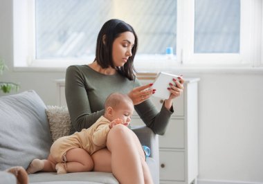 Evde doğum sonrası depresyon geçiren tablet bilgisayarı ve bebeği olan genç bir kadın var.