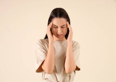 Bej arka planda baş ağrısı çeken genç bir kadın.