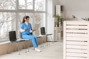 Klinikte dizüstü bilgisayar kullanan kulaklıklı Afro-Amerikalı bir stajyer.