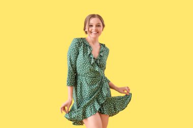 Güzel, genç, mutlu bir kadın sarı arka planda dans ediyor.