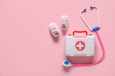 Pembe arka planda çocuk ayakkabısı ve steteskop olan ilk yardım çantası. Üst görünüm