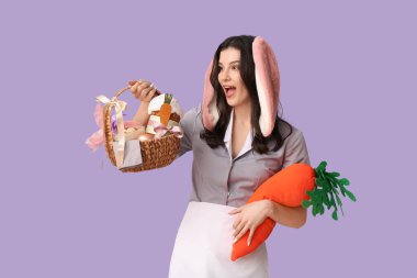 Paskalya sepeti ve mor arka planda oyuncak havuçla tavşan kulaklı kadın oda hizmetçisi şok oldu.