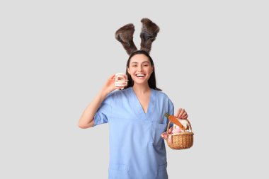 Tavşan kulaklı mutlu kadın dişçi Paskalya sepeti ve gri arka planda çene modeli